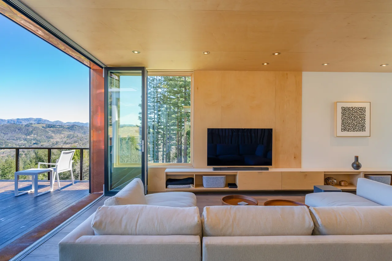Living room with wood-paneled media wall, sectional sofa, and large glass doors opening to a deck with mountain views.