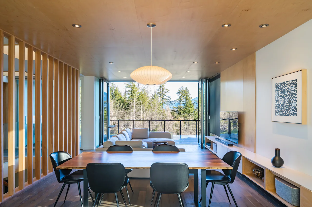Open plan dining and living area with wood accents and large folding glass doors opening to an outdoor space.