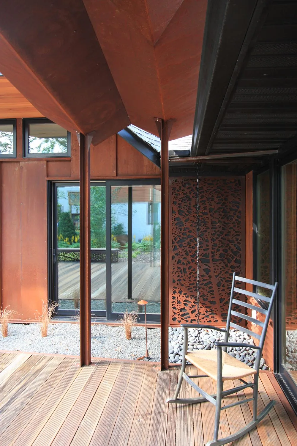 Wooden deck with a metal rocking chair and weathered metal siding features part of the folded roof design.