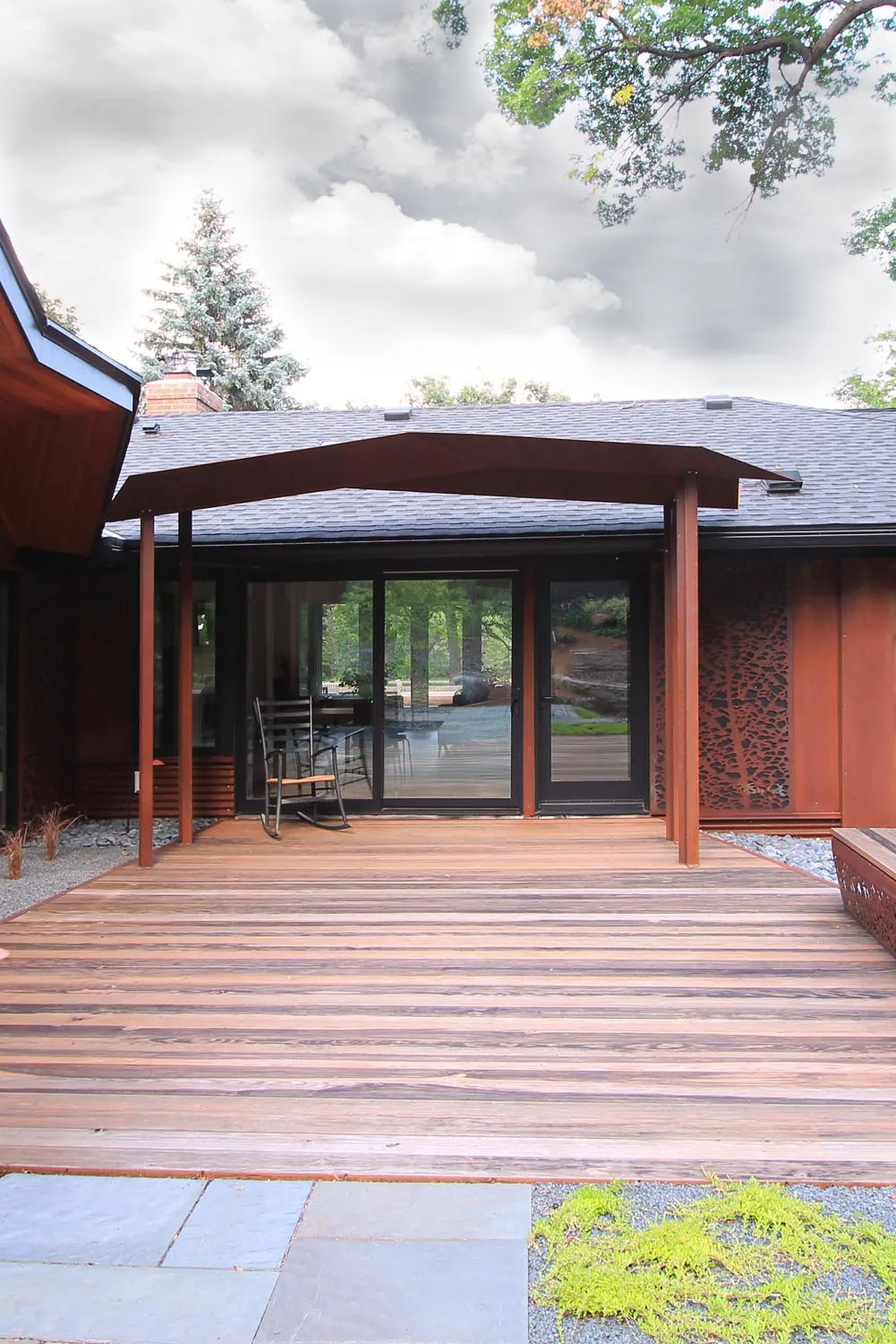 Folded House exterior shows a weathered wooden deck and covered patio with black-framed sliding glass doors.