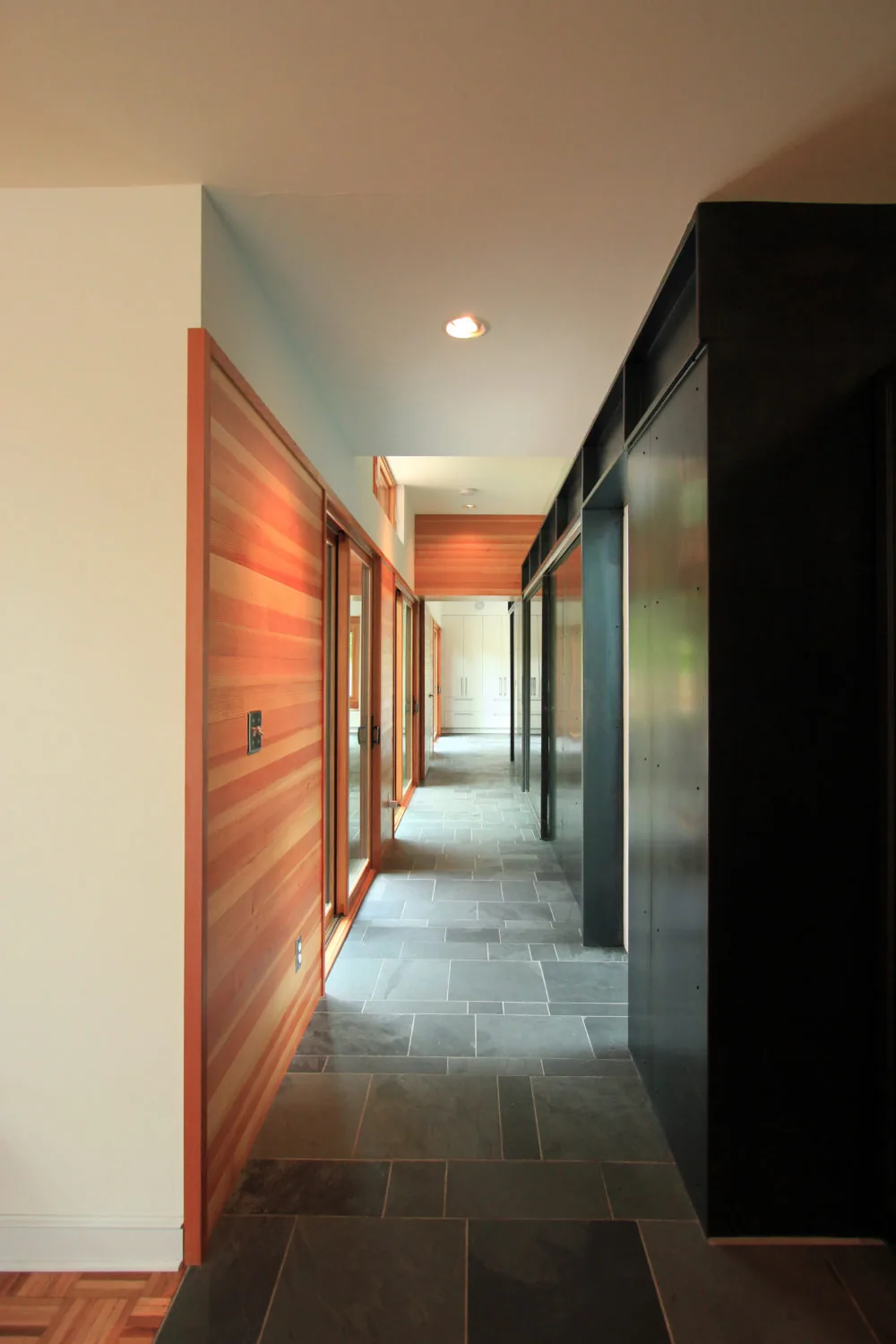 Hallway featuring slate tile flooring, horizontal wood siding wall with windows, and a black metal paneled wall.