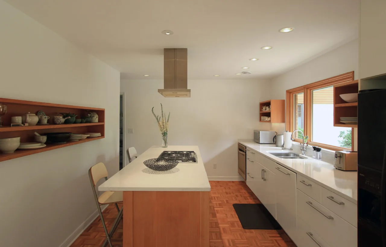 Kitchen interior featuring a white island with cooktop, wooden parquet floor, and open shelving for dishes and pottery.
