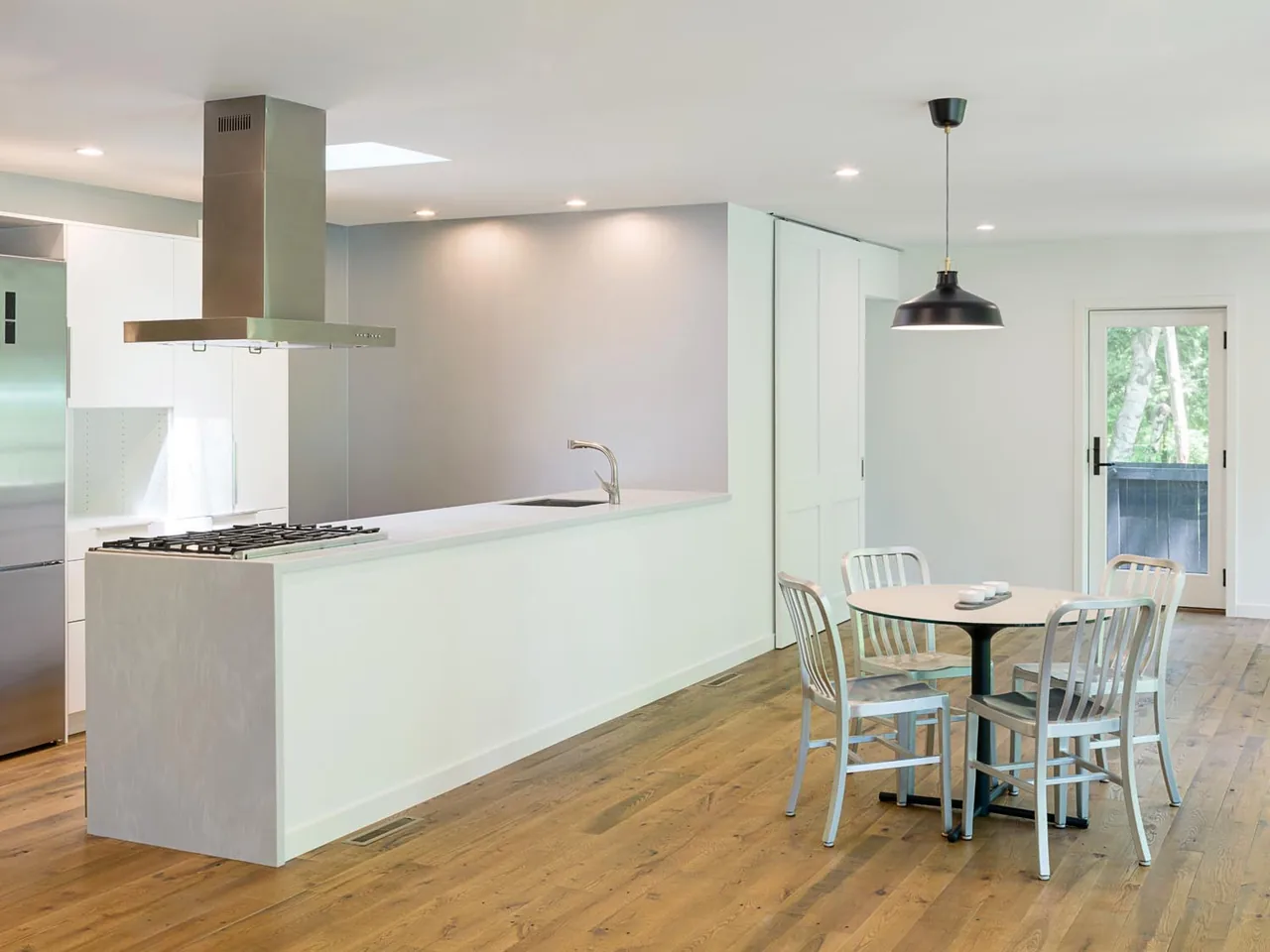 Kitchen and dining area with a stainless steel range hood, gas cooktop, and round dining table under a pendant light.