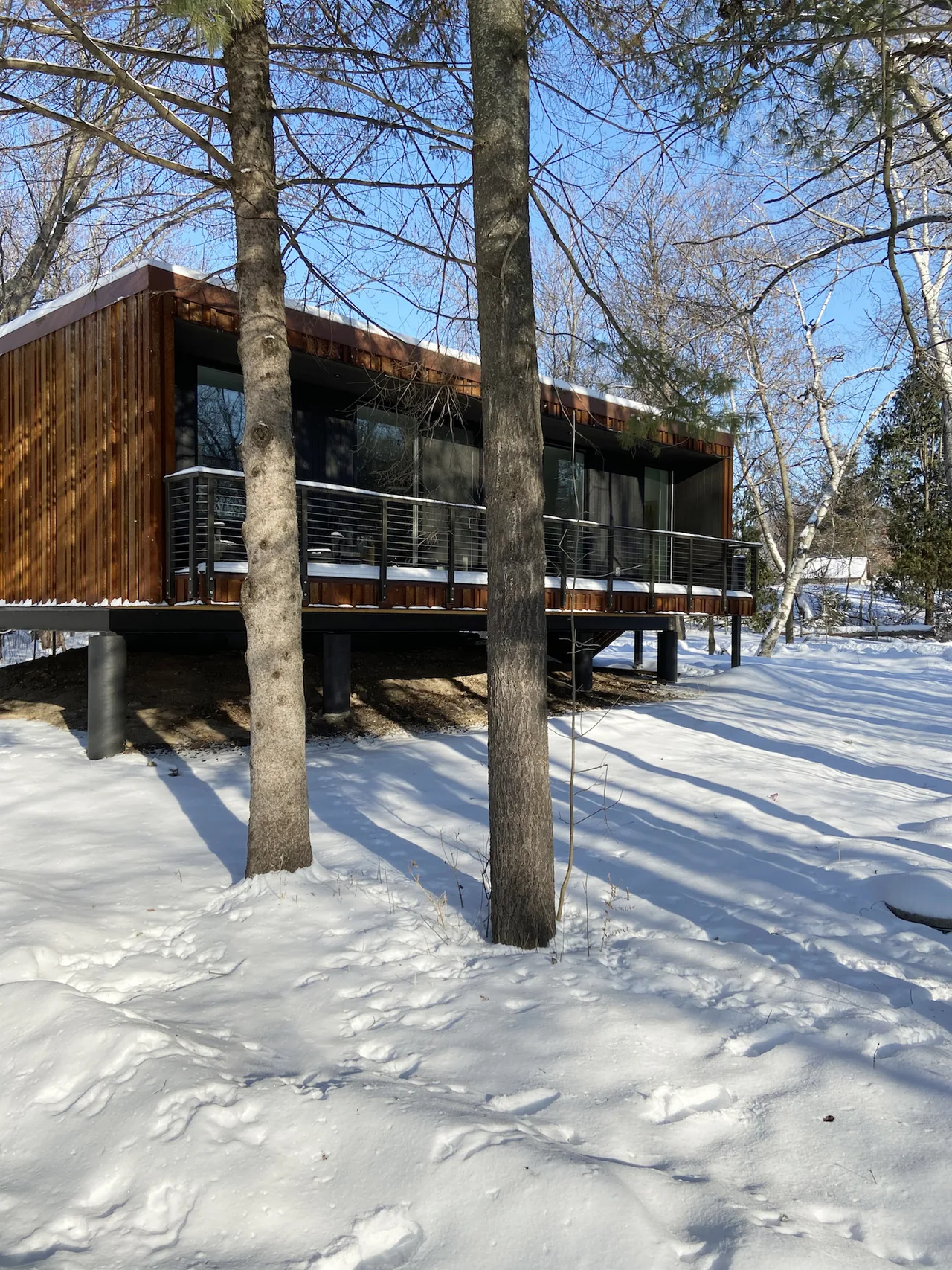 Elevated modern house with wood siding and metal railings on a snowy site.