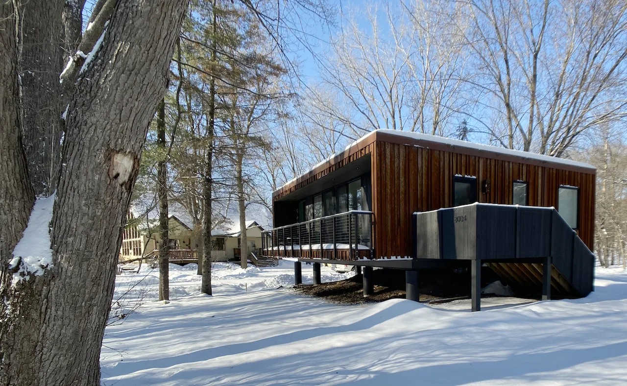 Elevated weeHouse with wood siding and flat roof in a snow-covered wooded setting.