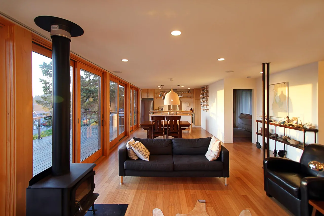 Open living and dining area with wood floors and large glass doors to a wooden deck at the Oceanside weeHouse project.