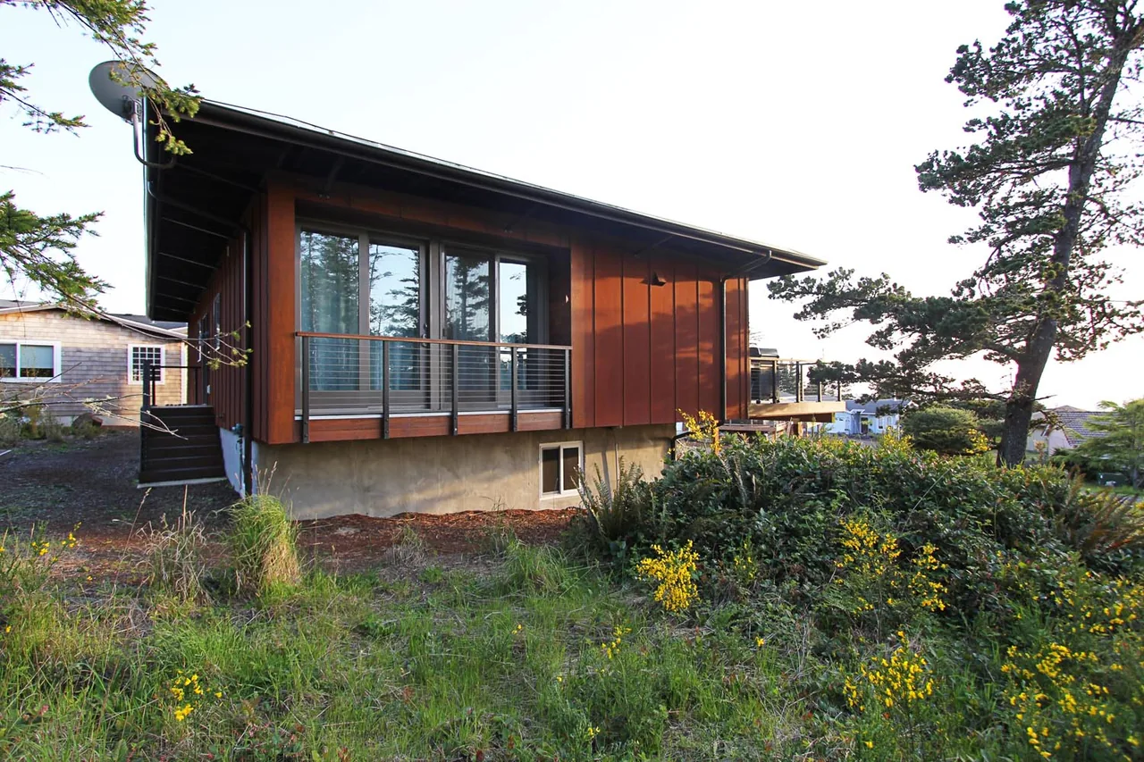 Oceanside weeHouse by Alchemy Architects features wood siding and a cable railing balcony over a concrete foundation.