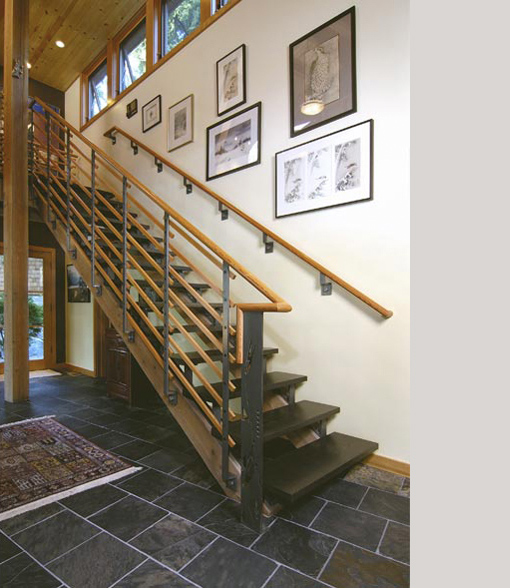 Open-riser stair with wood handrails and metal balusters beside a gallery wall in the Borth House entryway.