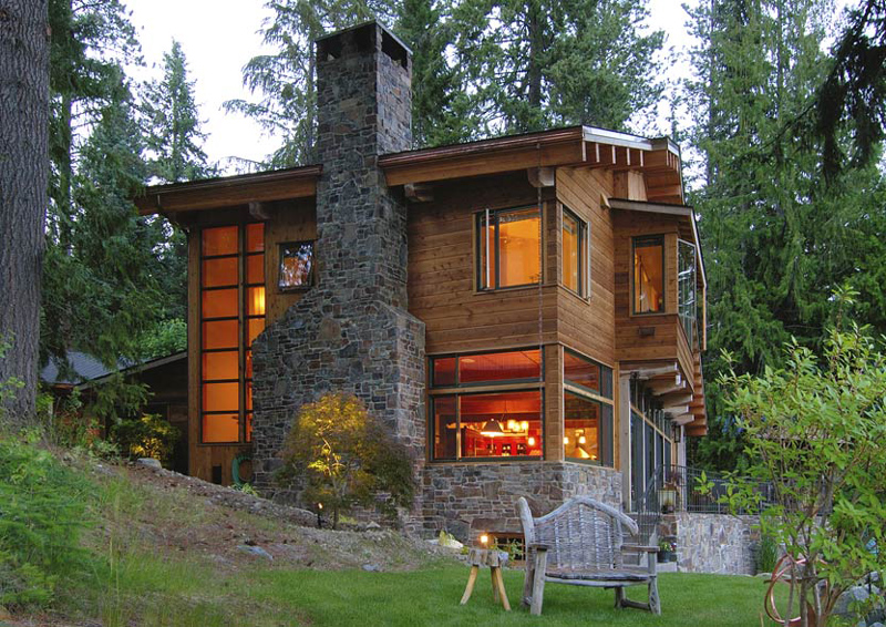 Exterior rear view of a two-story house with stone and wood cladding and a prominent stone chimney.