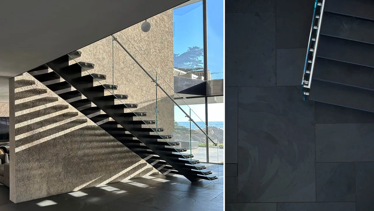 Floating black metal staircase with glass railing at Dogleg Residence by Lundberg Design in San Francisco, featuring textured stone walls and coastal views.