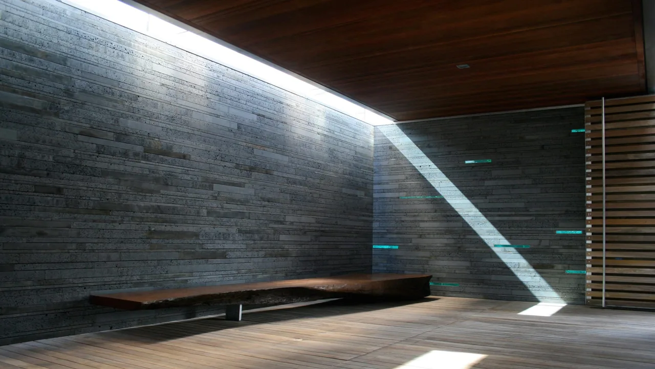 Interior corner with concrete plank walls, a clerestory window casting light, and a floating wooden bench.