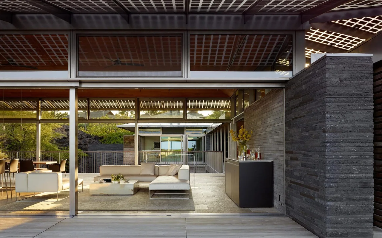 Outdoor living area with sliding glass doors, a sectional sofa, and a dining table on a stone tile floor, adjacent to a dark stone wall.