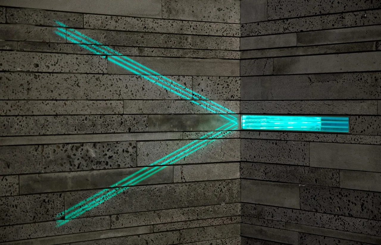 Narrow horizontal window in a textured stone wall casting blue light patterns in an interior corner.