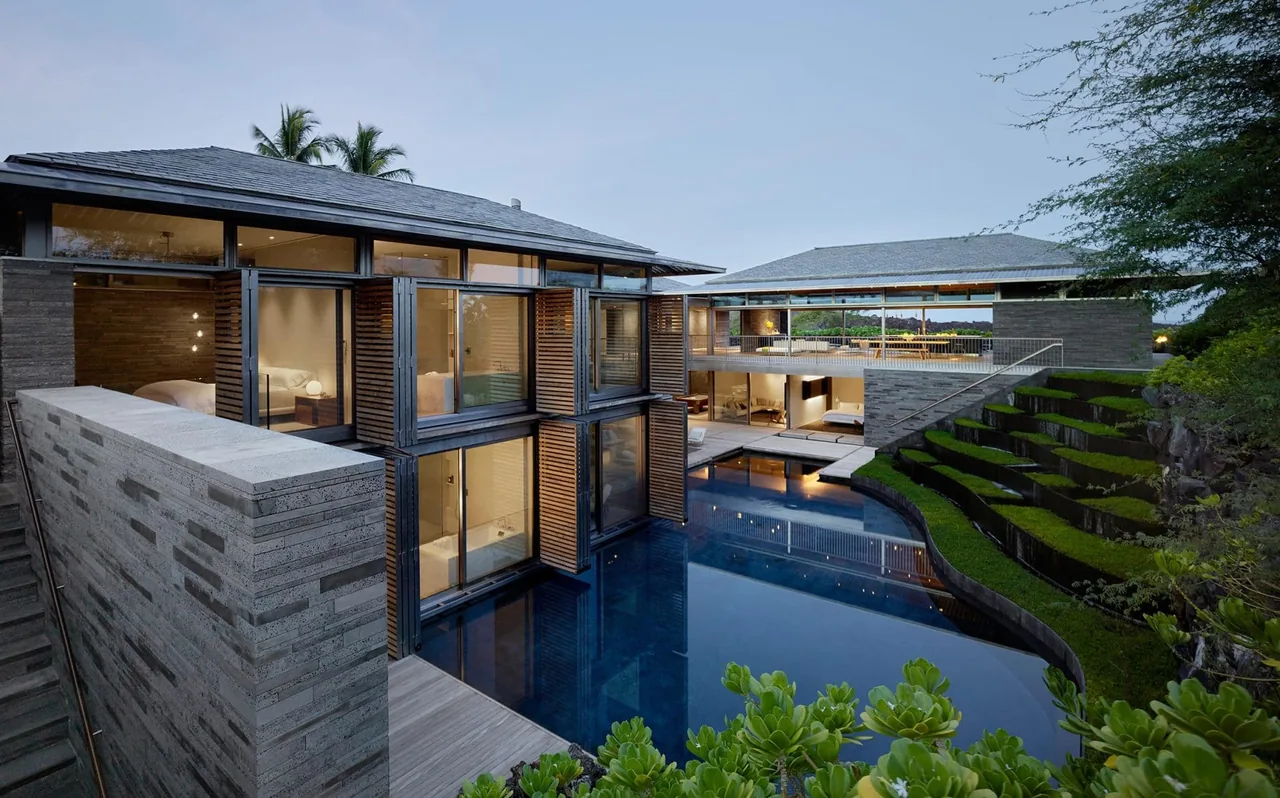 View of a modern residence featuring floor-to-ceiling glazing, wood shutters, concrete walls, and a reflecting pool with terraced landscaping.