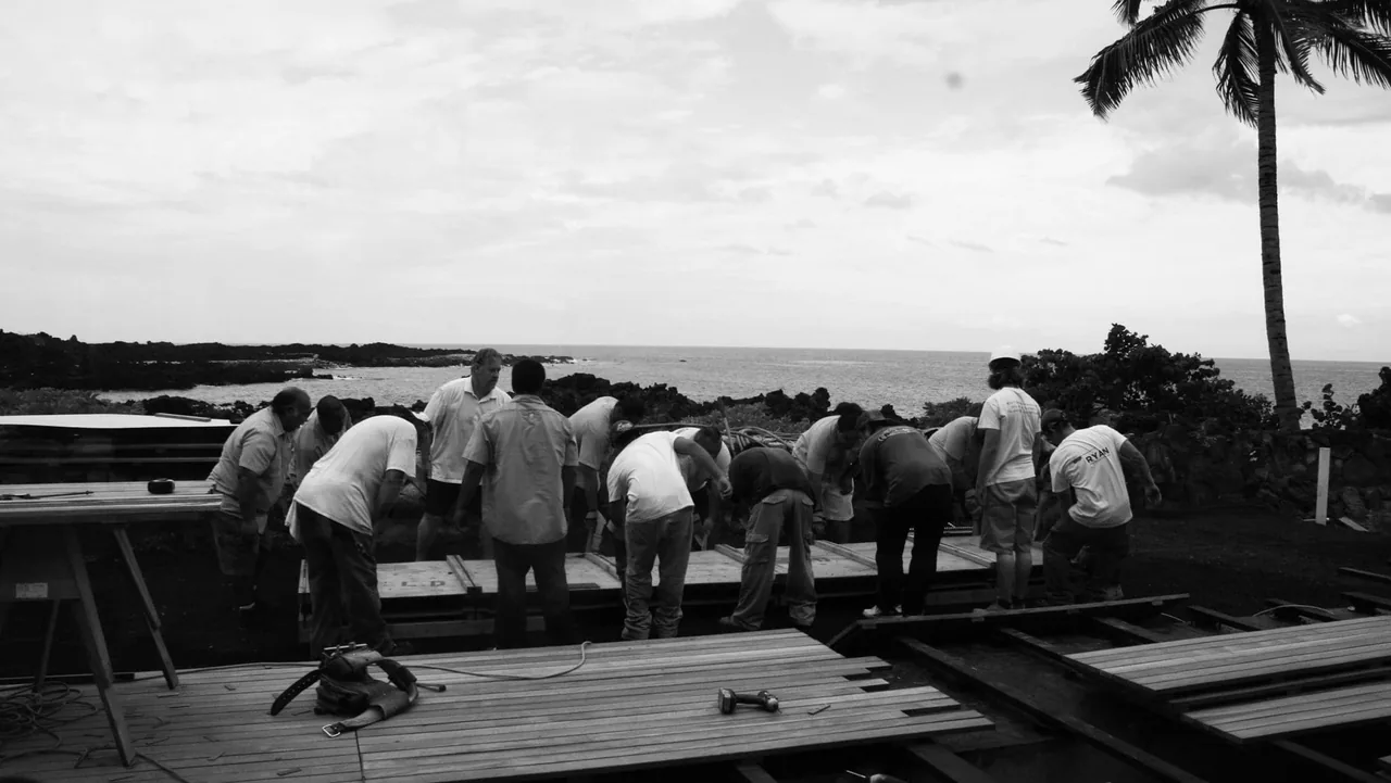 Construction workers together positioning wooden deck panels on frame by the ocean.