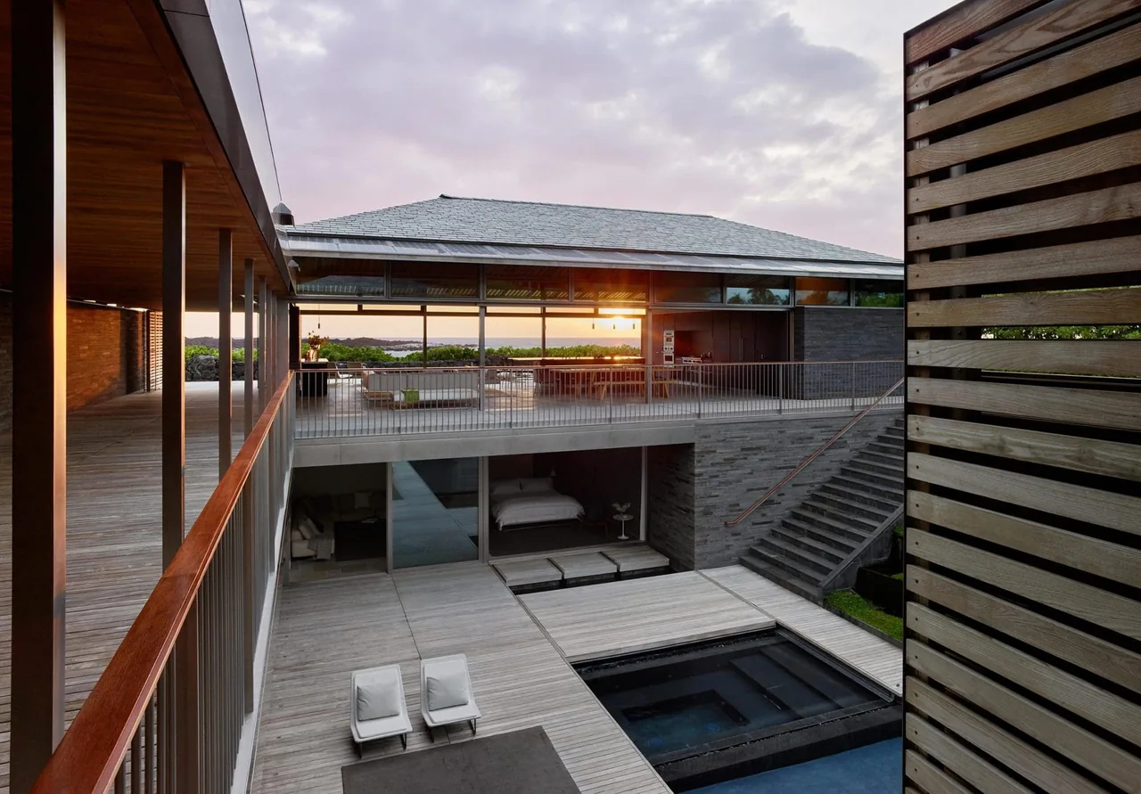 Multi-level modern residence with a courtyard pool, outdoor furniture, and panoramic water views at sunset.