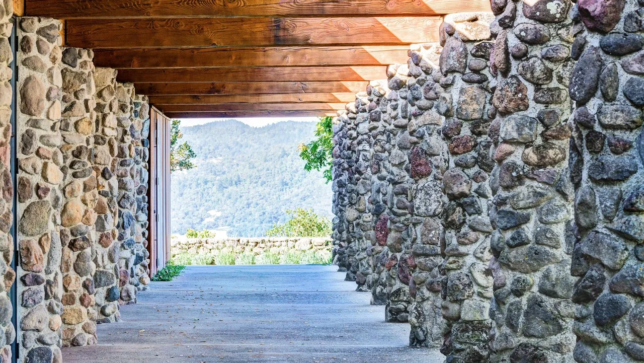 Stone-walled covered walkway with wood beam ceiling framing a mountain landscape at Napa Residence.