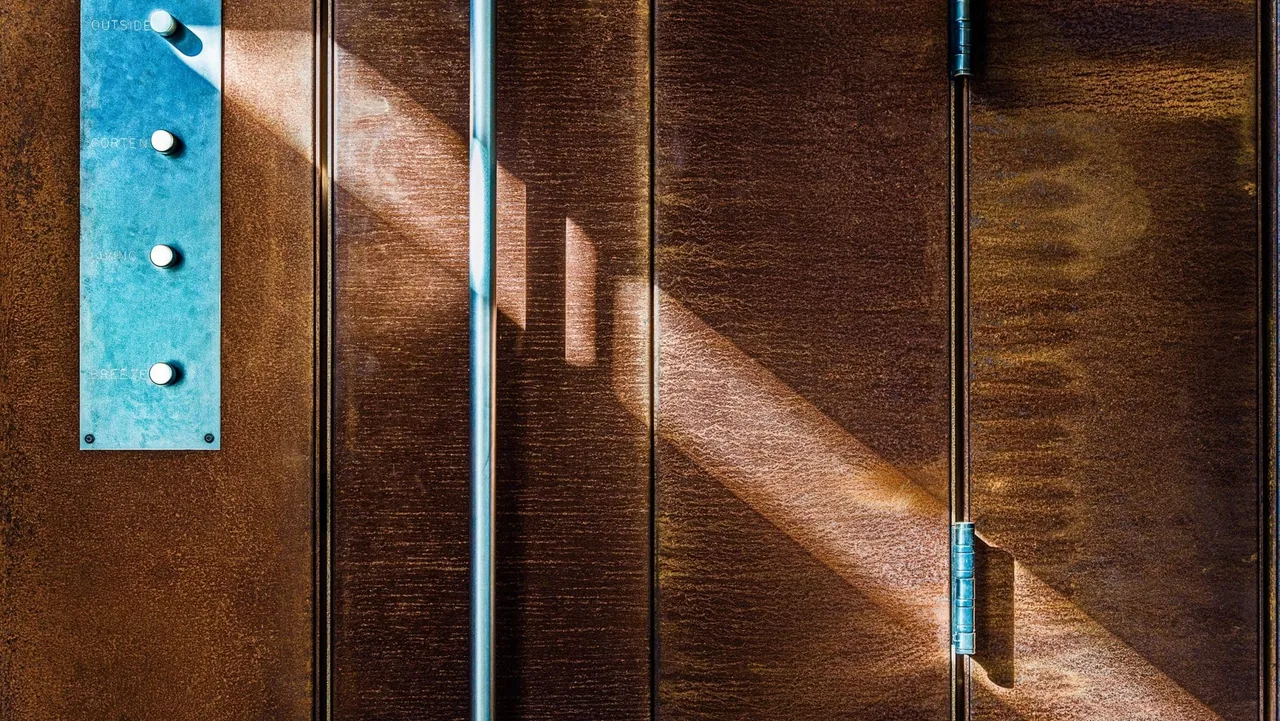 Door with a vertical metal handle and blue button panel, featuring textured rust-colored surface.