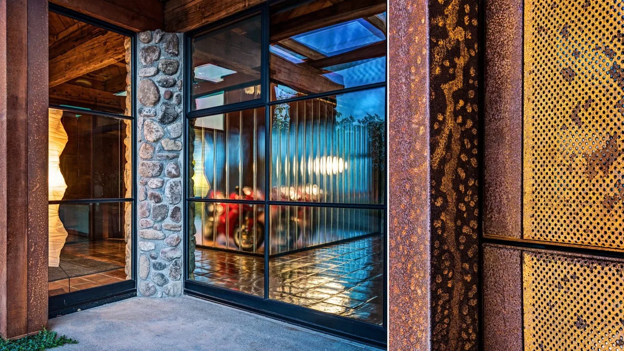 Exterior corner of Napa Residence features stone columns, weathered metal siding, black-framed glass walls, and exposed wooden beams.