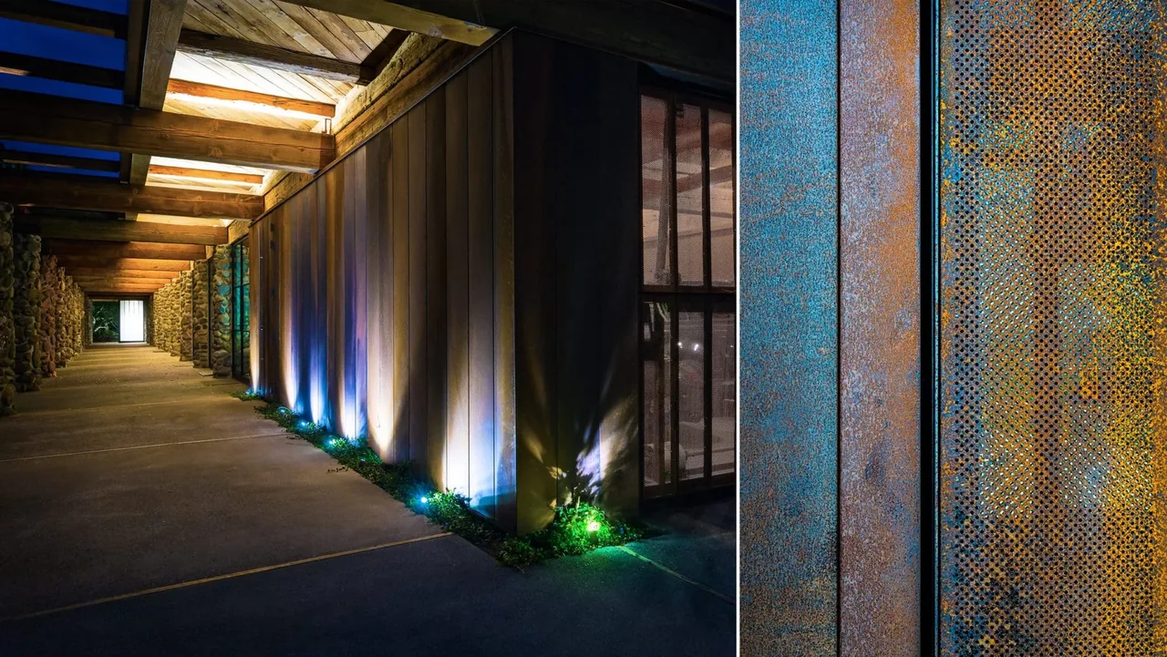The Napa Residence features a covered outdoor hallway with a wooden beam ceiling and rusted metal panels illuminated by ground lighting.