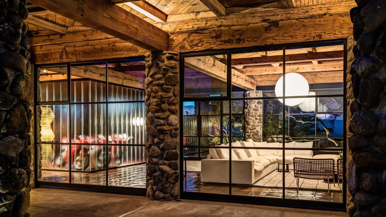 Napa Residence living room features stone columns, wood beam ceiling, and floor-to-ceiling black-framed windows at night.