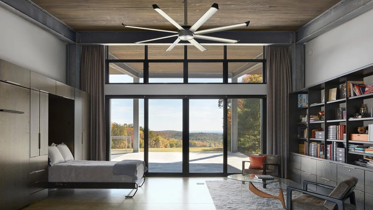 Bedroom features large floor-to-ceiling glass doors and transom windows, with a view of the open landscape beyond a concrete patio.