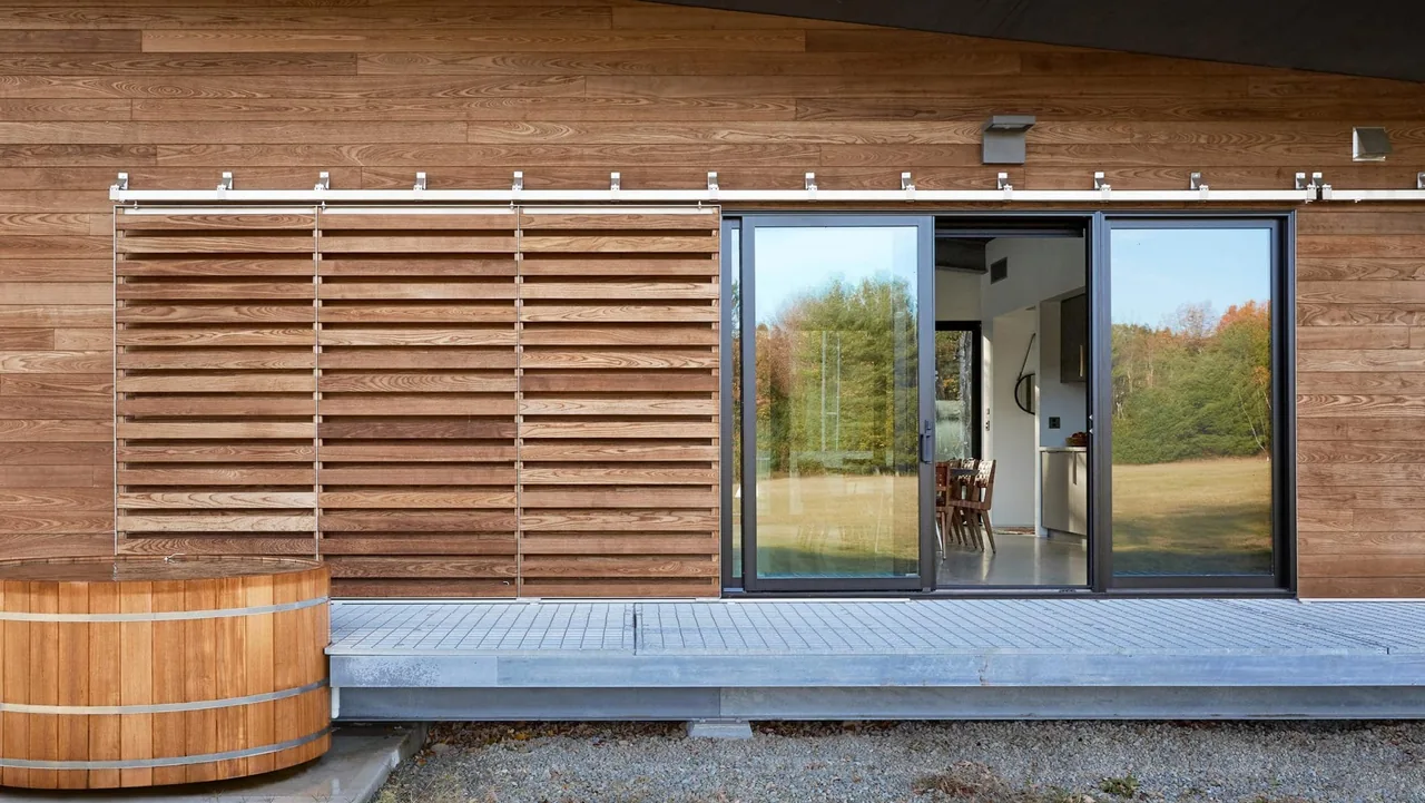 Wall section with horizontal wooden siding, sliding glass doors in black frames, and a metal platform with a wooden barrel planter outside.