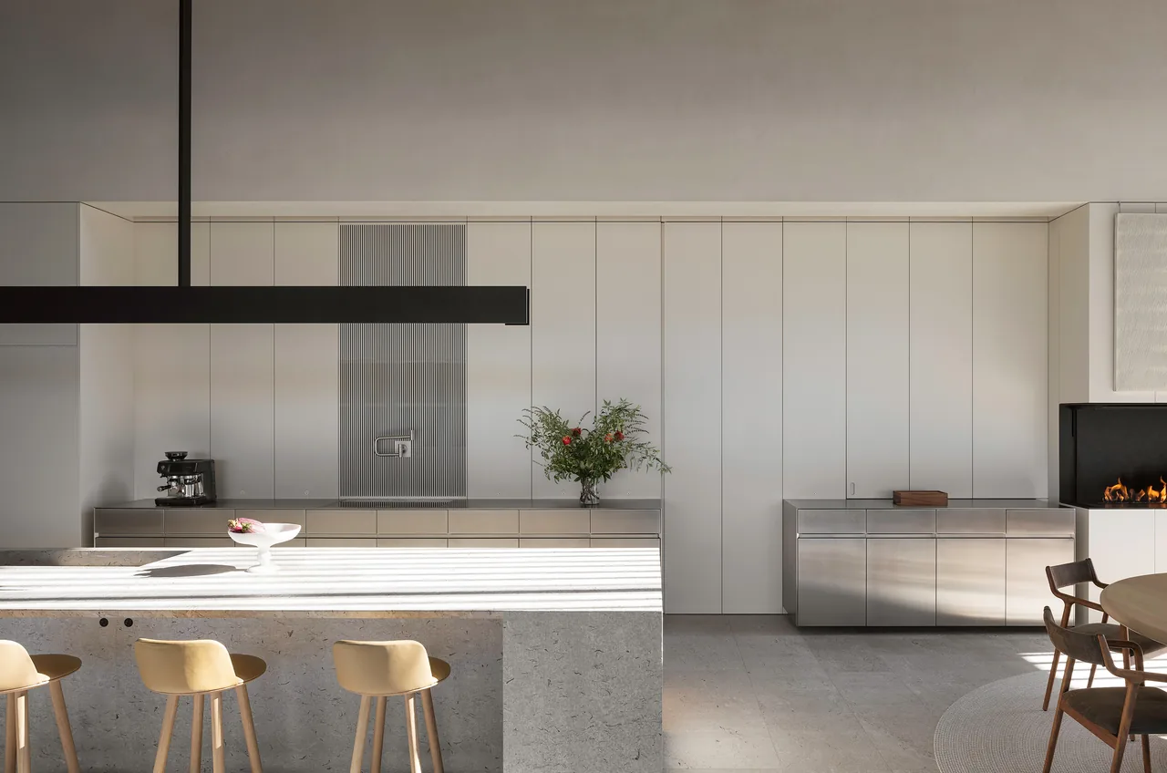 Kitchen featuring a concrete island, minimalist cabinetry, and a built-in coffee machine and faucet set into white panel walls.