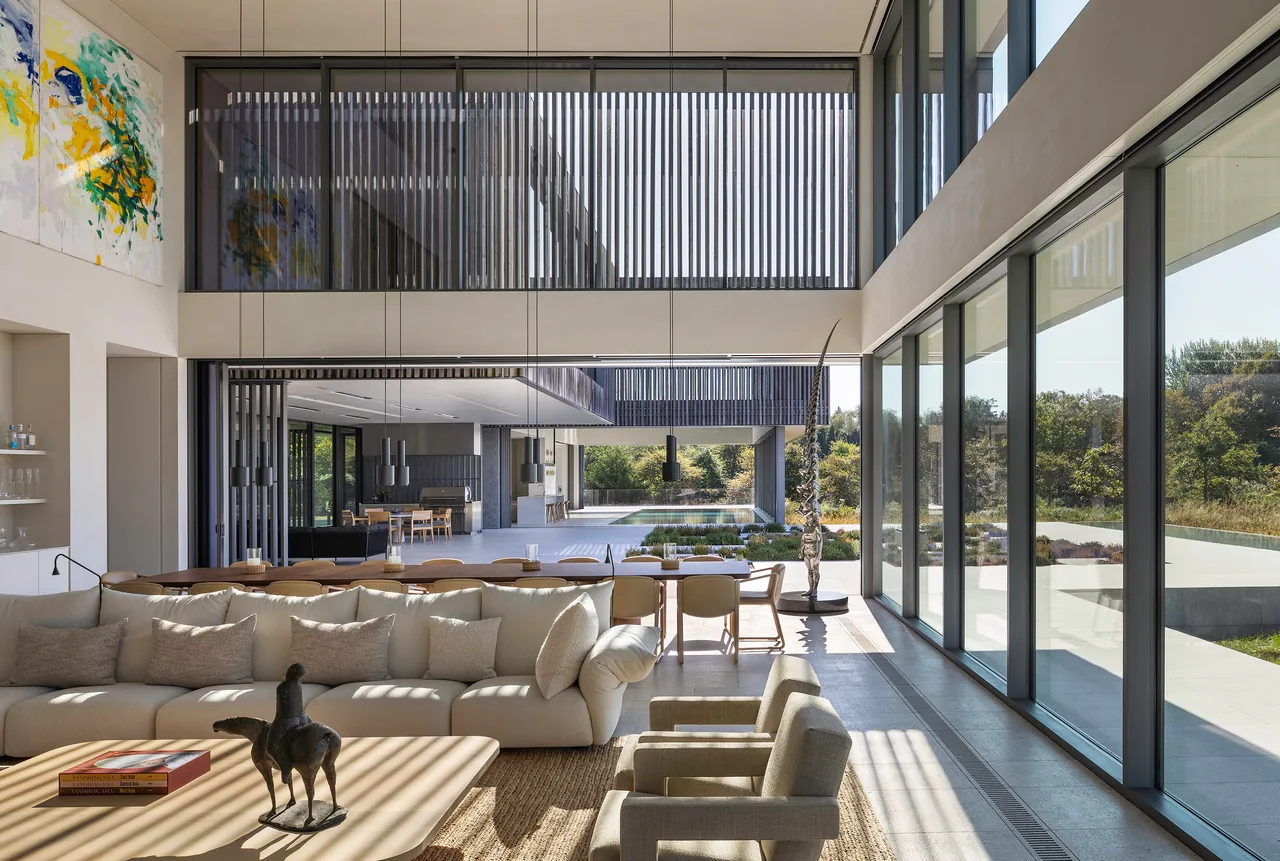 Living and dining area with large glass walls opening to an outdoor space in the Shinnecock project.