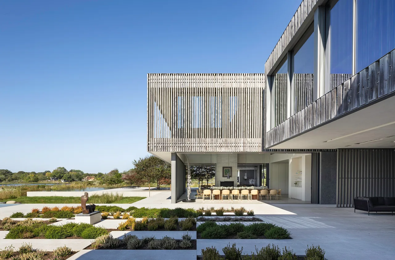 Exterior view of a modern house featuring wood slats on the upper level and large glass panels on the lower level, with a landscaped garden in the foreground.
