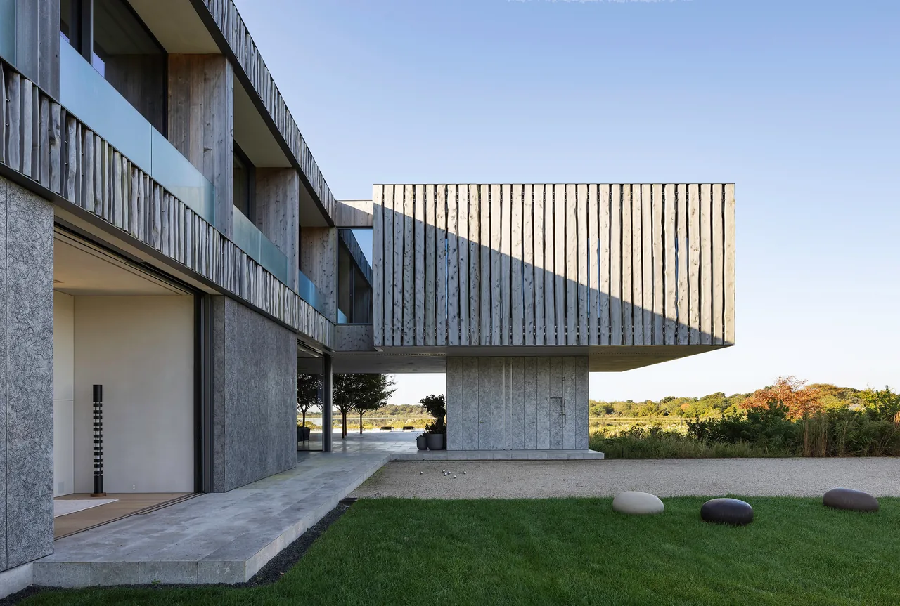 Exterior view of a modern house showing cantilevered second floor with wood cladding and concrete ground floor facade.