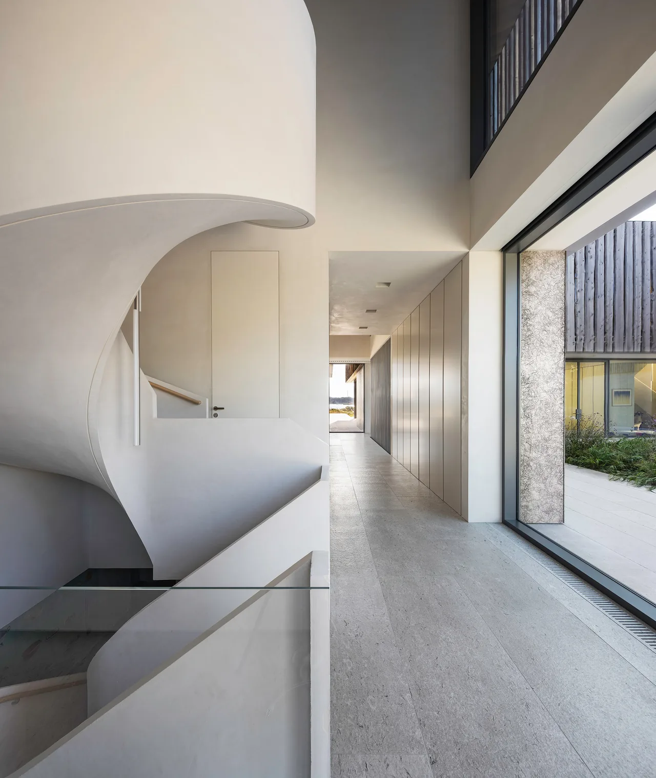 Hallway featuring a sculptural curved staircase and large glazing with views to an exterior courtyard.