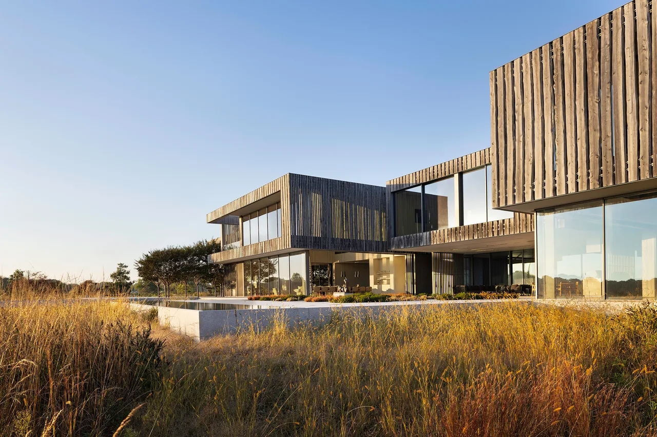 Modern house exterior with vertical wood siding and extensive glazing in a natural grassy setting.