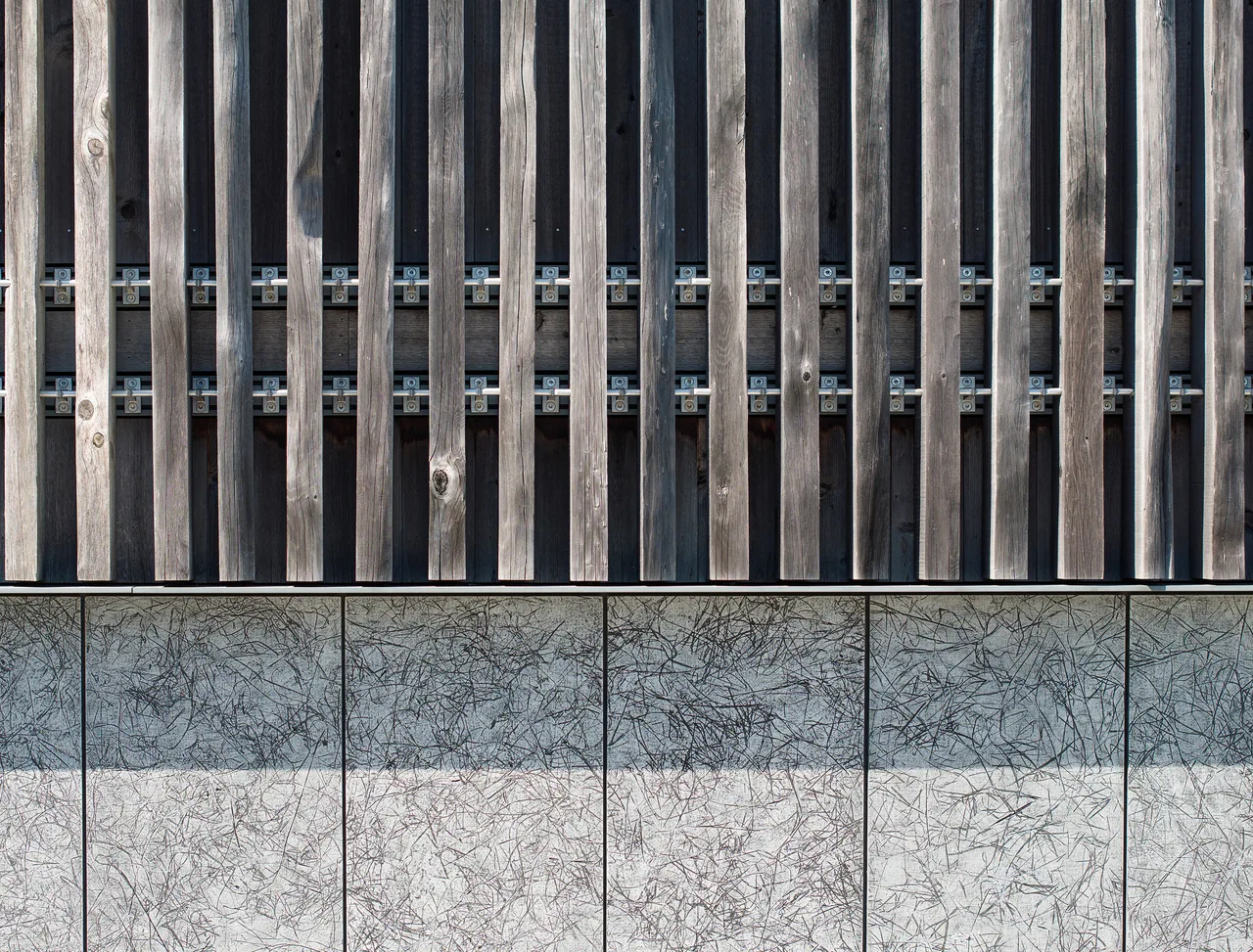 Detail of facade combining vertical wood slats and textured concrete panels held by metal brackets.