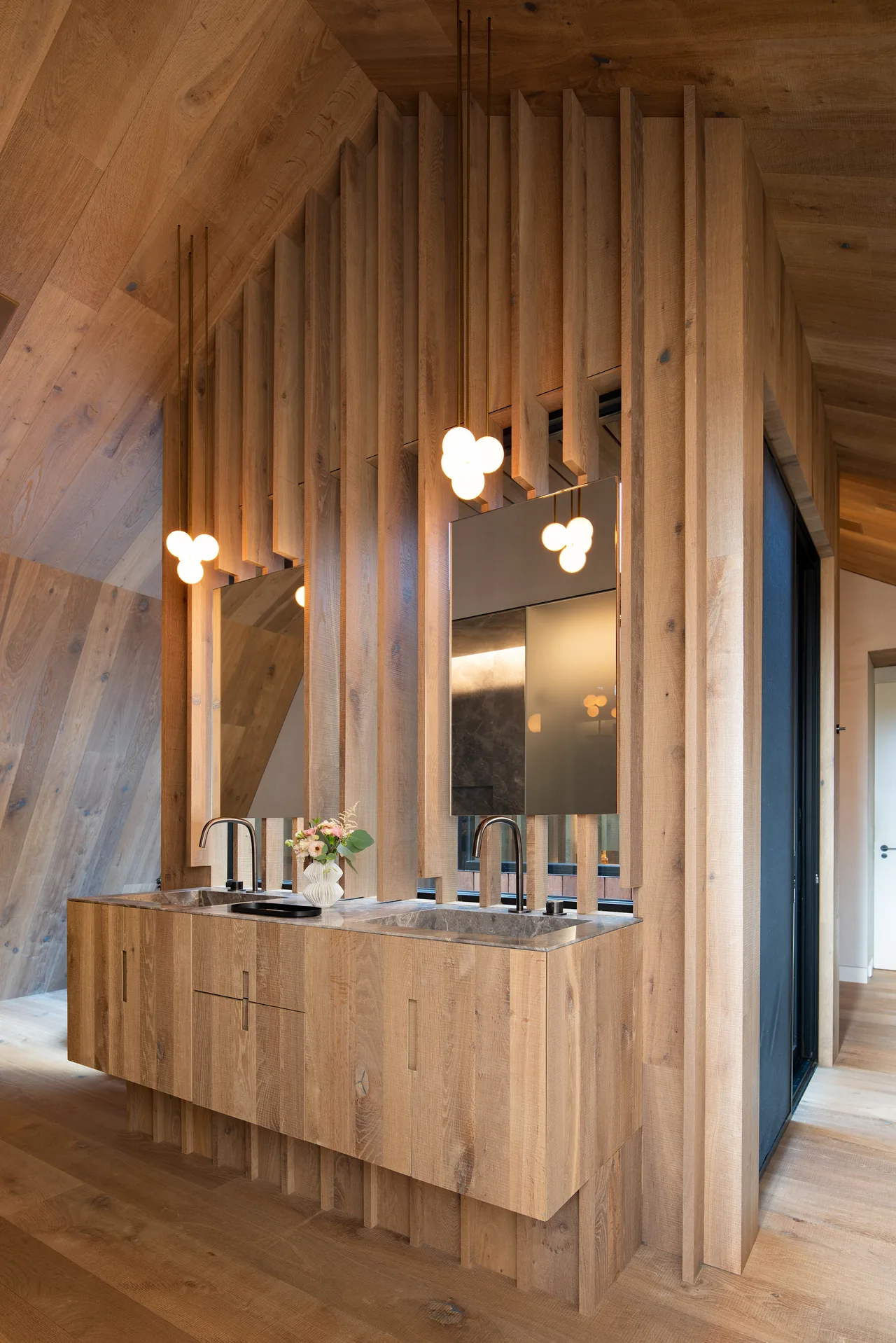 Bathroom vanity in wood with vertical slat partition and bubble pendant lights above double sinks.