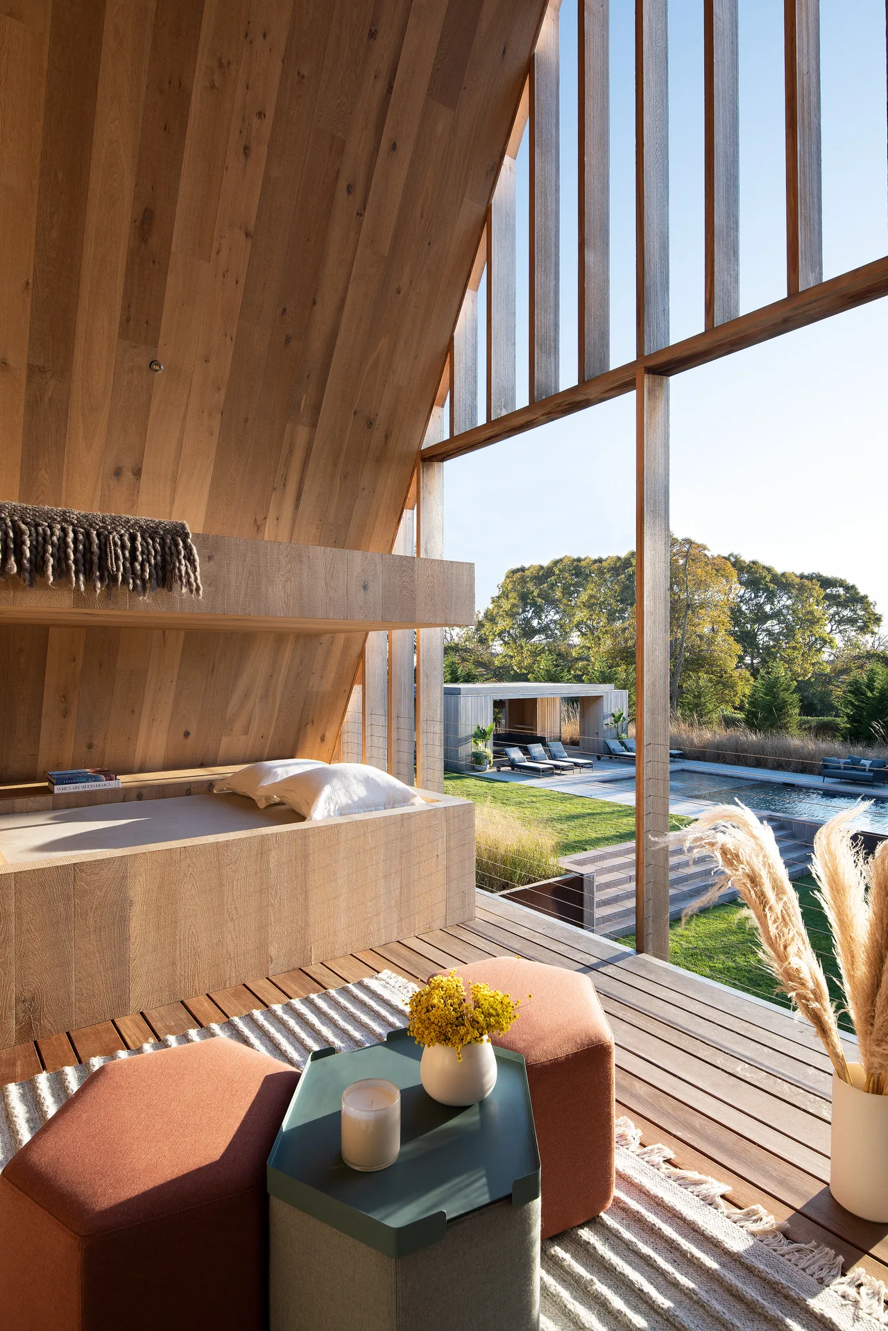 Wood-paneled lounging area with built-in bench features expansive vertical wood-framed windows opening to a pool and garden outdoors.