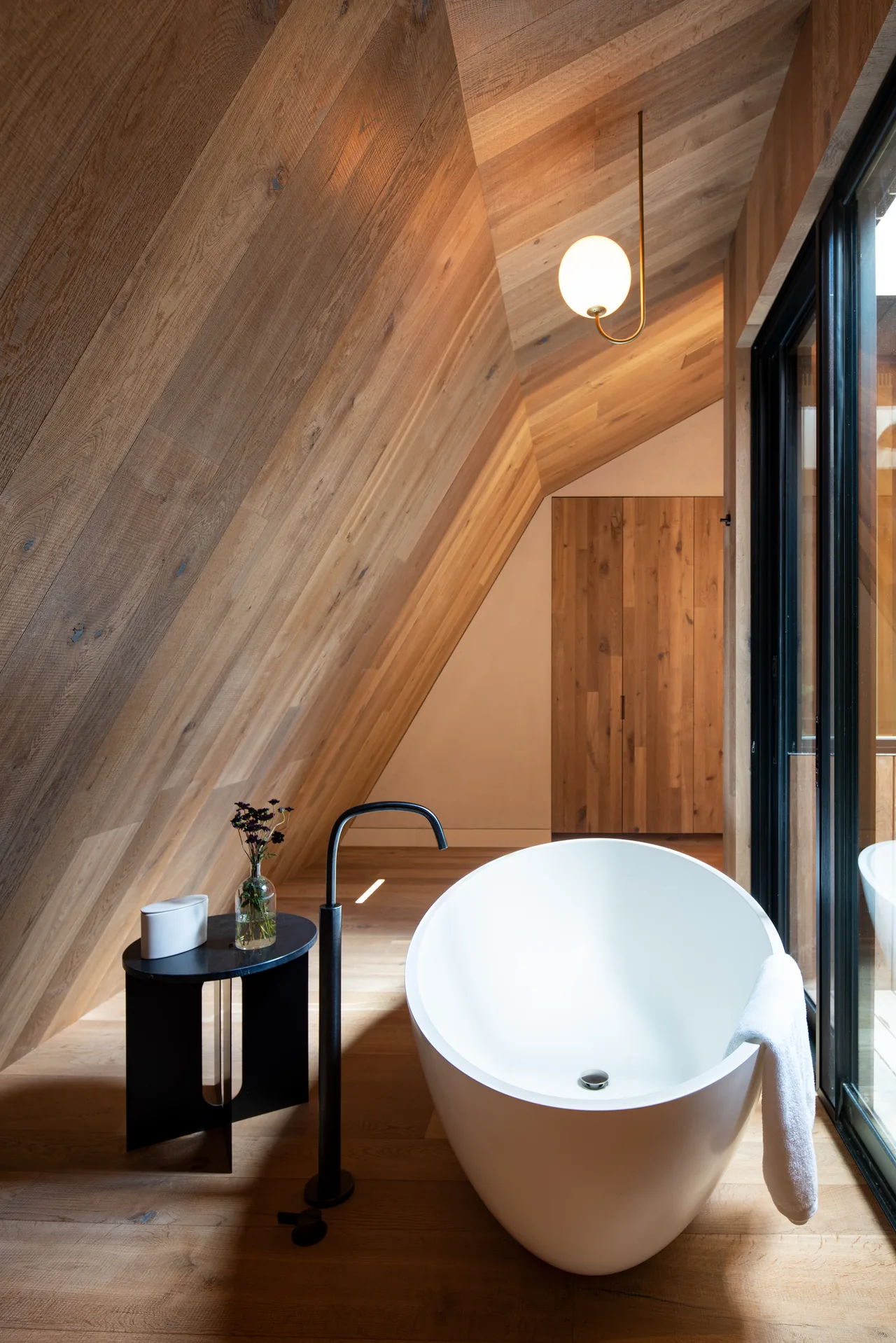Wood-paneled bathroom featuring a white freestanding tub and black floor-mounted faucet under a sloped ceiling.