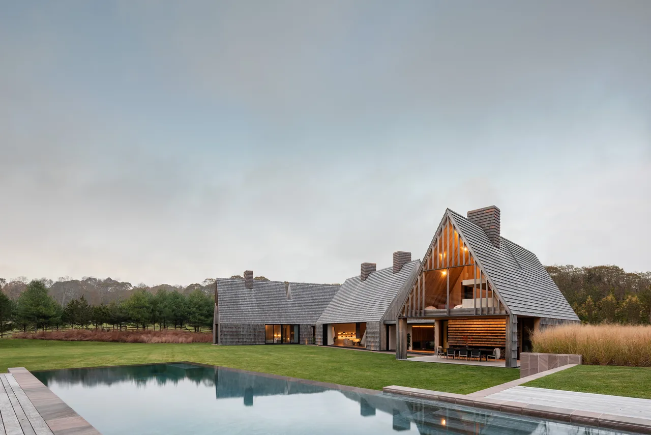 The Stony Hill house by Bates Masi Architects features steep pitched wood shingle roofs and open outdoor living spaces next to a pool.