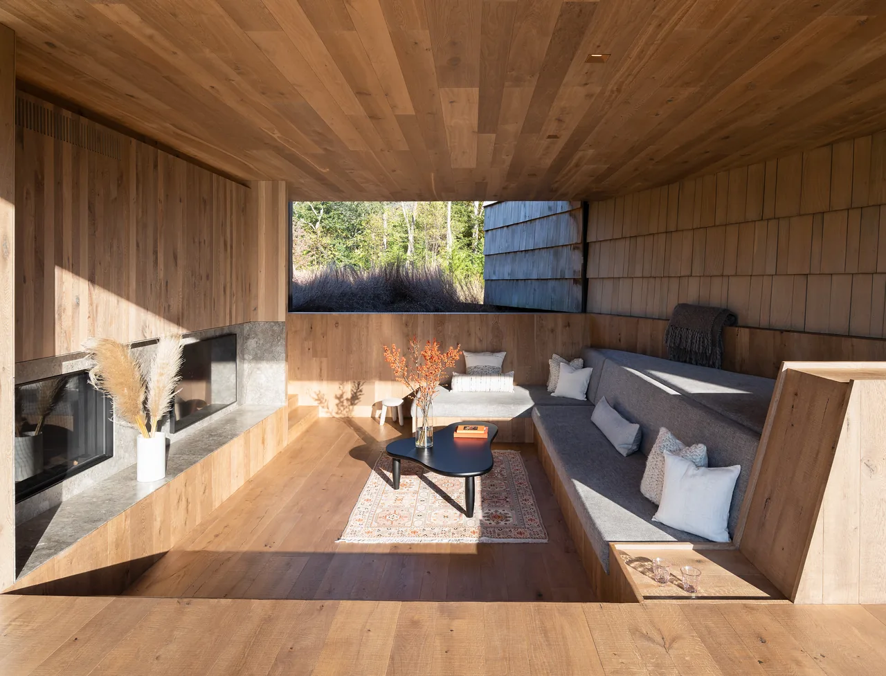 Living area with built-in L-shaped seating, wood-paneled walls and ceiling, and a stone fireplace at Stony Hill project.