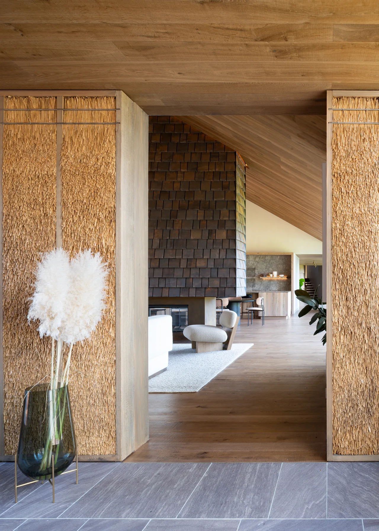 Entryway with textured panel walls and stone tile floor leads to living space featuring a wood-paneled fireplace and vaulted ceiling.