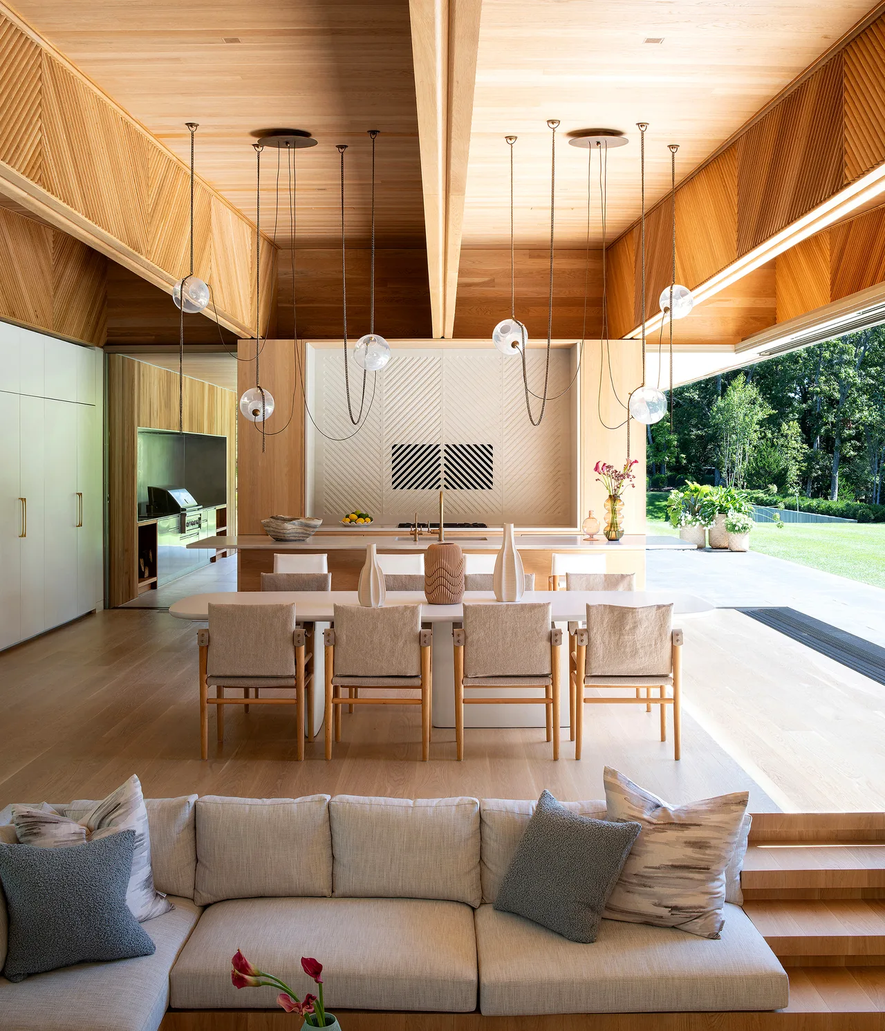 Open-plan living and dining area featuring wood paneling, pendant lighting, and large sliding glass doors to an outdoor space.