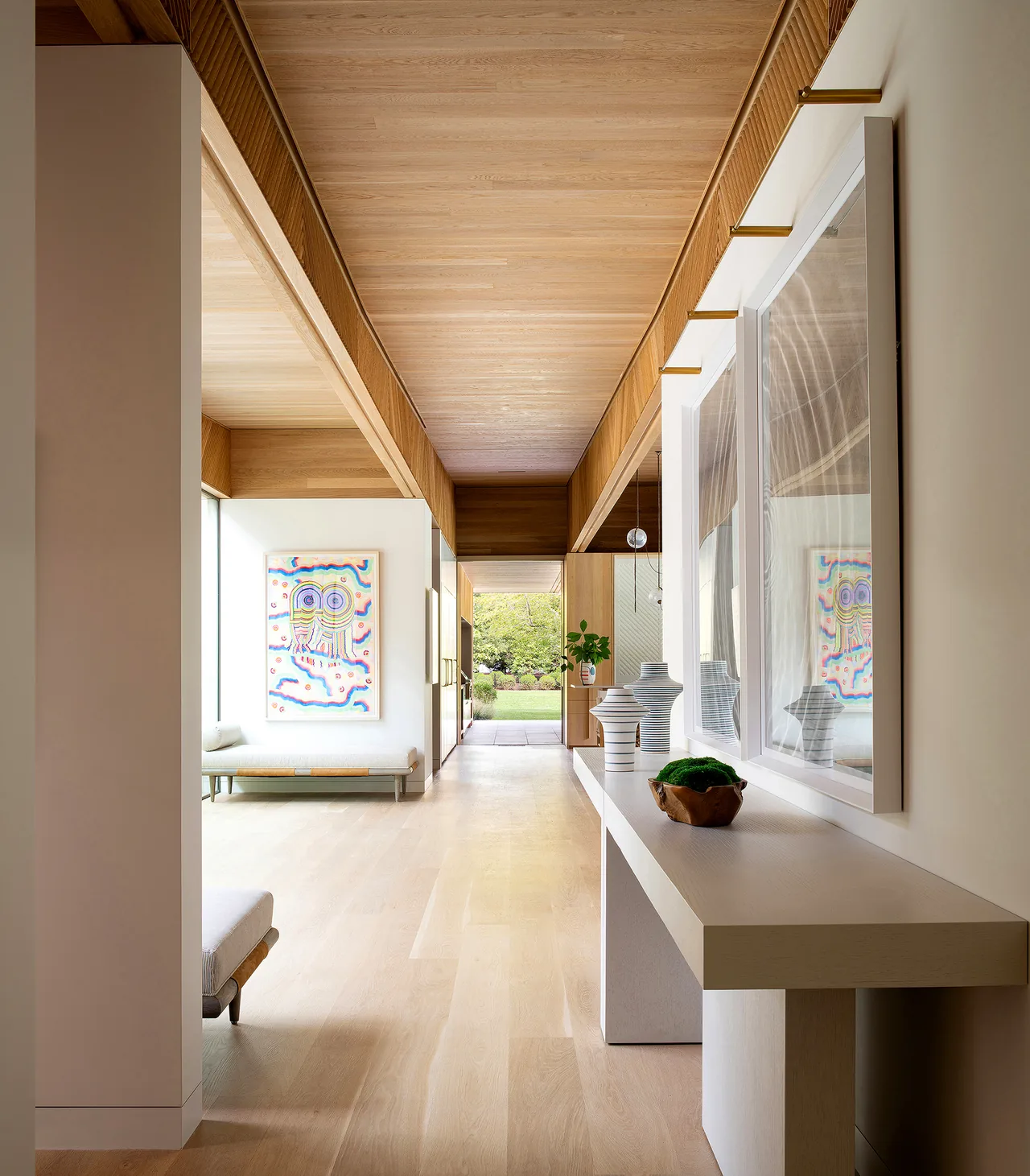 Interior hallway featuring a wood ceiling and light hardwood floor with artwork and decorative items on the console table.