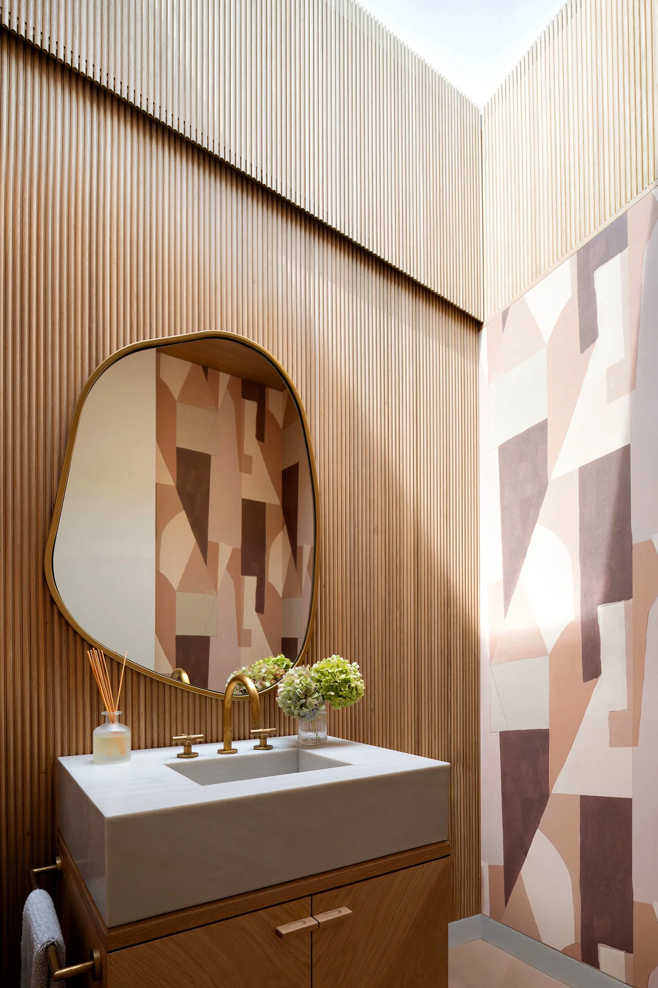Powder room featuring vertical wood slat walls, an abstract mural, brass fixtures, and a stone sink.