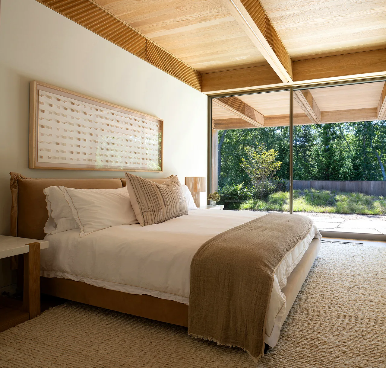 Bedroom with floor-to-ceiling sliding glass doors that open to an outdoor area and ceiling with wood beams and slatted panels.