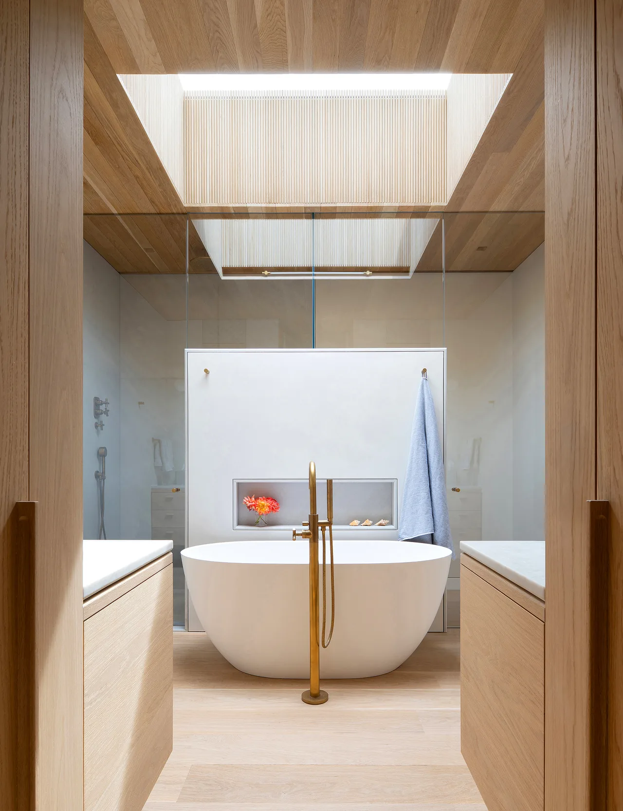 Bathroom featuring a freestanding tub, brass fixtures, light wood finishes, and a skylight.