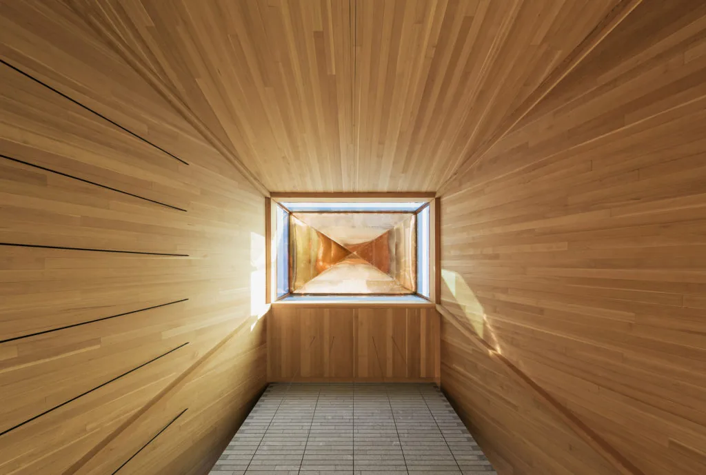 Square skylight set in wood-paneled ceiling with copper interior and surrounding wood walls.
