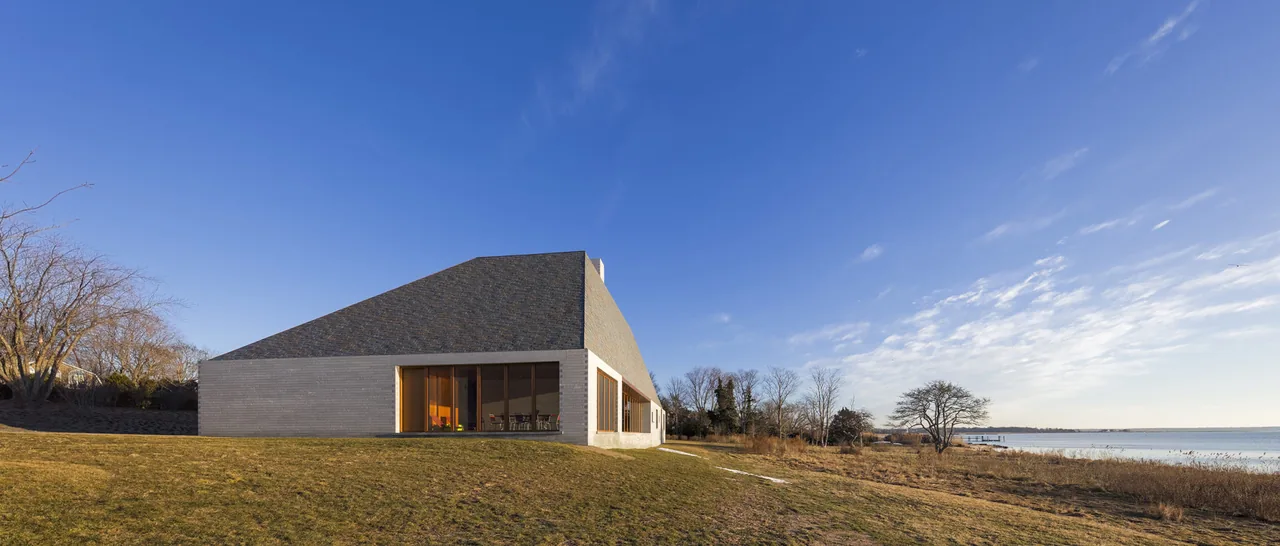 Side exterior of a modern Bayhouse with sloped roof and floor-to-ceiling glazing facing the waterfront.