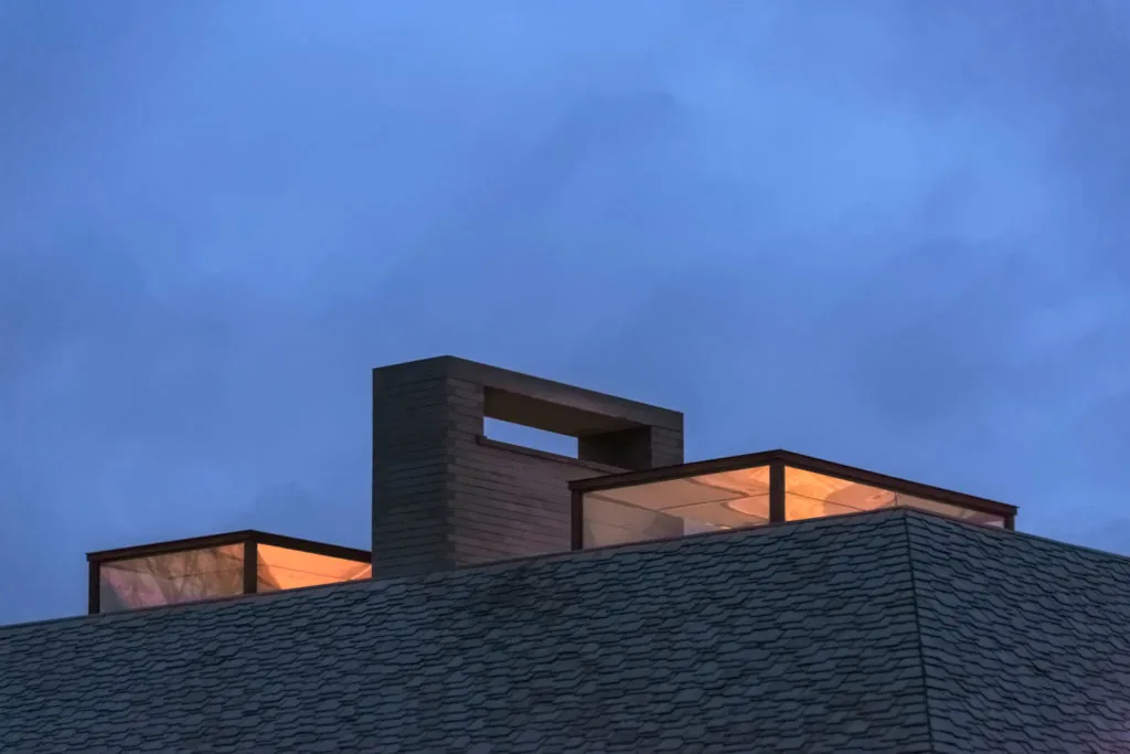Skylight structures and a chimney rise from a textured roof against a dusk sky.