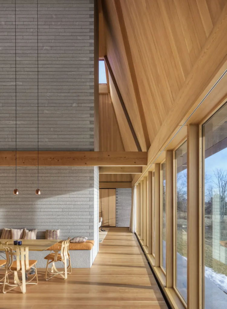 Dining area with wooden furnishings and extensive floor-to-ceiling glazing in a wood-paneled interior.
