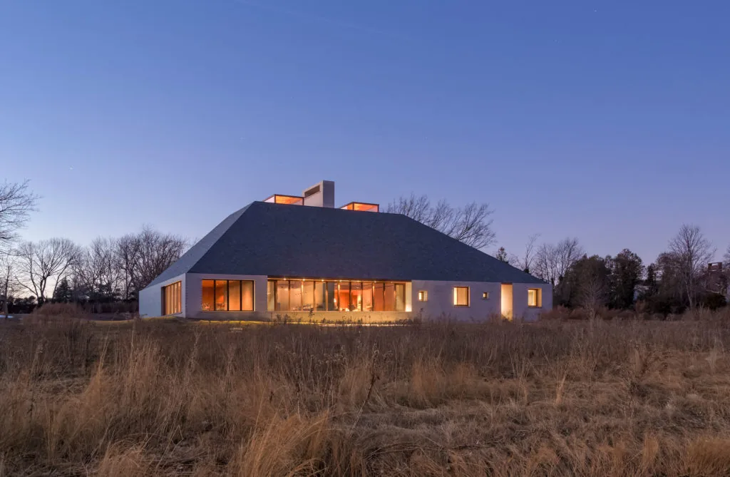 Dusk exterior front view of Bayhouse showing the illuminated windows and unique roof shape.